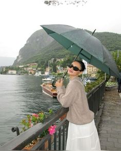 a woman holding an umbrella over her head while standing next to the water with boats in the background