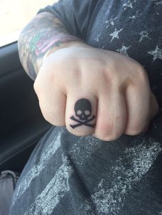 a person with a skull and crossbone tattoo on their finger