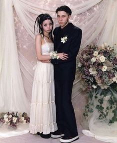 a man and woman standing next to each other in front of a flower covered wall