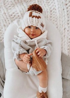 a baby is wearing a hat and holding a mitt while laying on a blanket