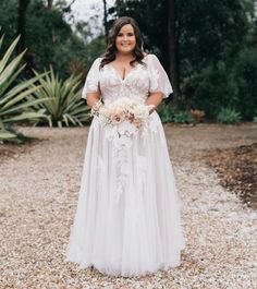 a woman in a white wedding dress standing on gravel with her hands in her pockets