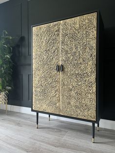 a black and gold cabinet with two doors on each side in front of a potted plant