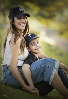 a beautiful young woman sitting next to a boy wearing a baseball cap and jeans on the grass