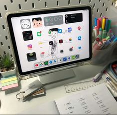 a computer monitor sitting on top of a desk next to a pile of pens and pencils