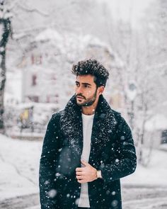 a man standing in the snow wearing a black jacket and white sweater with his hands on his hips