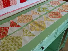 a green table topped with lots of quilts on top of it's sides