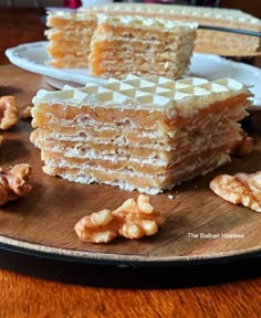 a stack of cake sitting on top of a wooden cutting board next to a plate with walnuts