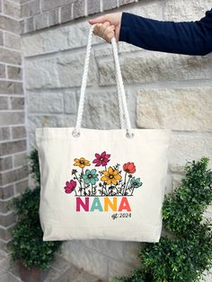 a person holding a white bag with flowers on it and the words nana written in multicolored letters