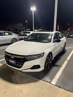 a white honda accord is parked in a parking lot at night with its lights on