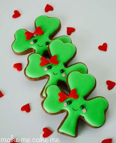 three decorated shamrock cookies sitting on top of a white table next to red heart shaped confetti