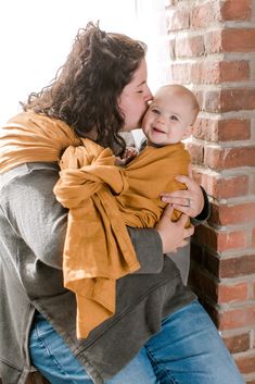 a woman holding a baby in her arms and kissing it's face against a brick wall