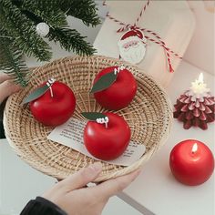 a person holding a basket with apples on top of it next to candles and a christmas tree