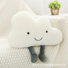 a white cloud pillow with a smiling face on it sitting on a couch next to a potted plant