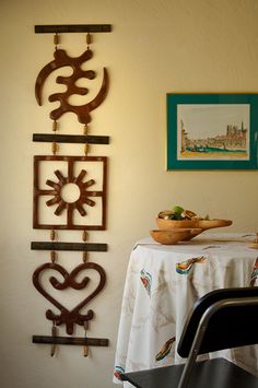 a dining room table with a bowl of fruit on it next to metal wall art