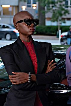 a man in a black suit and sunglasses standing next to a car with his arms crossed