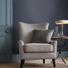 a chair with a pillow on it in front of a blue wall and floor lamp