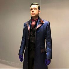 a man in a blue coat and purple gloves is standing next to a white wall