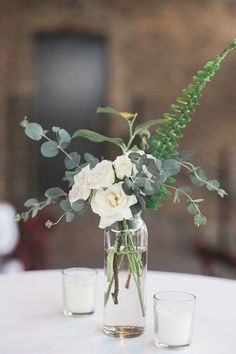 a vase filled with flowers and greenery sitting on top of a table next to two glasses