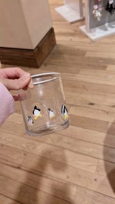 a person holding a glass with penguins painted on the side and inside it in front of a wooden floor