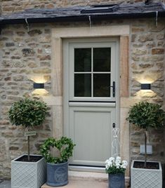 two planters are sitting in front of the door to a stone building with potted plants