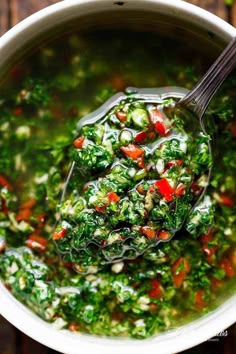 a ladle full of vegetable soup with spinach and red bell peppers in it