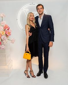 a man and woman standing next to each other in front of a wall with flowers