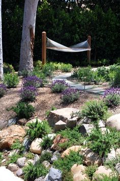 a hammock in the middle of a garden with rocks and plants around it