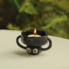 a black candle holder sitting on top of a white table next to a green plant