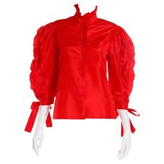 This vintage 1980's Louis Feraud Blouse is in a gorgeous red silk satin and features pretty ruffles and ties. This top has just the right amount of drama with a ruffled collar and red ball buttons down the center front. Each sleeve has three strips of ruffles going from the shoulders to the cuffs, which have pretty ties. This is the kind of blouse that adds depth to a wardrobe and it can be worn with so many separates from jeans to evening skirts! This blouse was originally purchased with a blac Black Ruffled Skirt, Vintage Bodysuit, Edwardian Blouse, Versace Style, Louis Feraud, Evening Skirts, Bodysuit Blouse, Ruffled Blouse, Red Ball