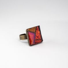 a square ring with an orange and red design on the front, sitting on a white surface