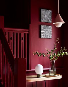 a vase with flowers on a table in front of a red wall and stair case