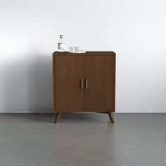 a wooden cabinet sitting on top of a floor next to a white wall with a vase