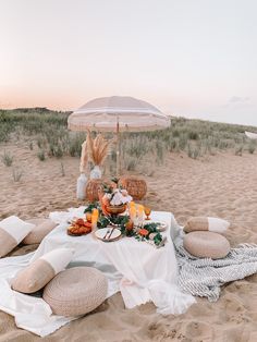 a table set up on the beach with food and an umbrella in the sand at sunset