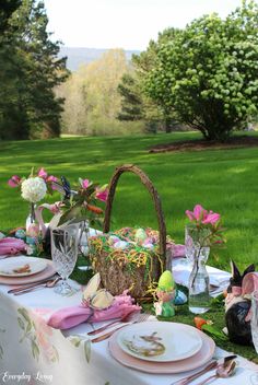 an outdoor table set for easter dinner with flowers and eggs in the basket on it