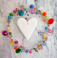 a white heart hanging from a metal chain with colorful beads around it on a wall