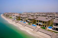 an aerial view of houses on the beach with swimming pool in foreground and blue water