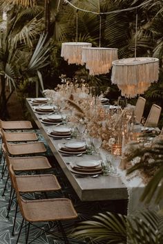 a long table is set with place settings and hanging chandeliers, surrounded by palm trees