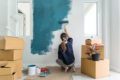 a woman is painting the wall with blue paint and she is kneeling on the floor