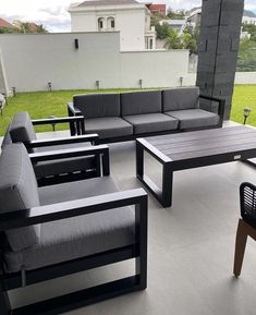 an outdoor seating area with grey couches and tables on the outside patio, next to a green lawn