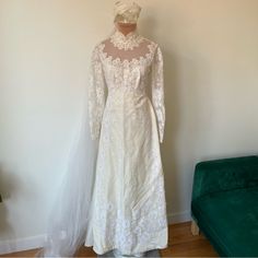 a wedding dress on display in front of a green velvet bench and white wall behind it