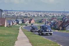 two old cars driving down the road in front of houses