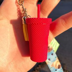 a hand holding a red plastic cup with a straw in it and a chain attached to it