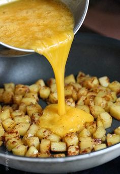 someone is pouring sauce on some food in a skillet with potatoes and other foods