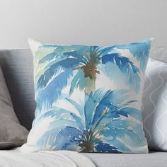 a blue and green palm tree print pillow on a gray couch with white throw pillows