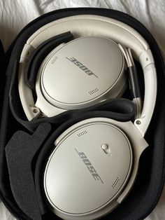 two white headphones in a case on a bed