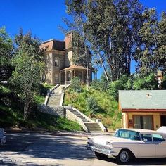 an old car is parked in front of a house on the side of a hill