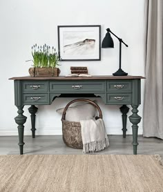 a desk with a lamp, potted plants and a rug on the floor in front of it