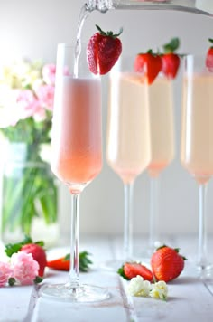 three glasses filled with champagne and strawberries on a table next to vases full of flowers