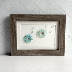 two blue flowers in a wooden frame on a white wall with herringbone tile behind it