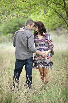 a man and woman standing in tall grass holding hands while looking at each other's eyes